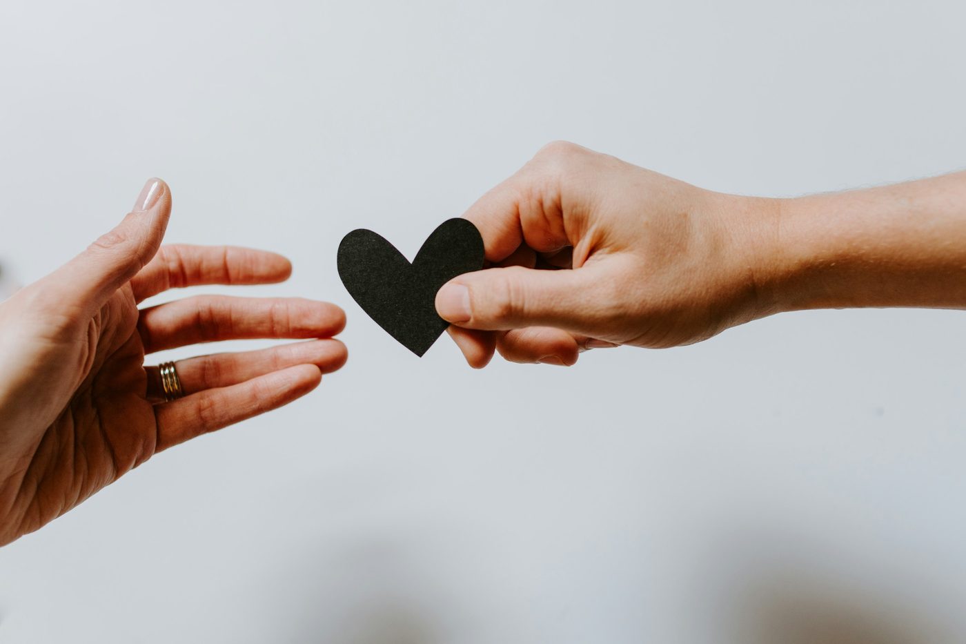 One hand offering a paper heart to another, symbolizing giving